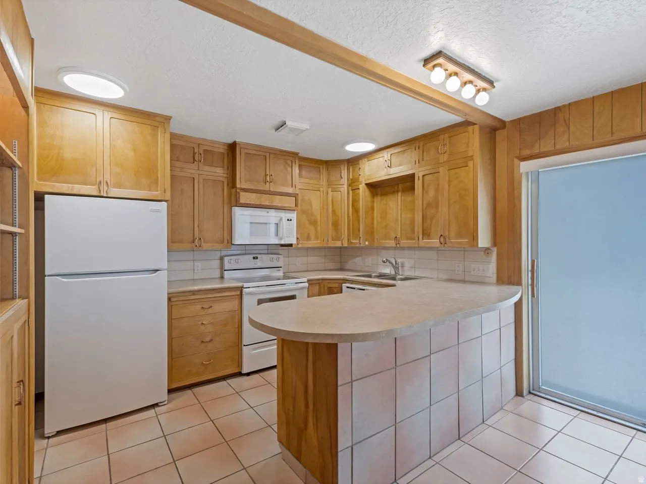Kitchen featuring light wood cabinetry, tiled countertops, and a curved breakfast bar