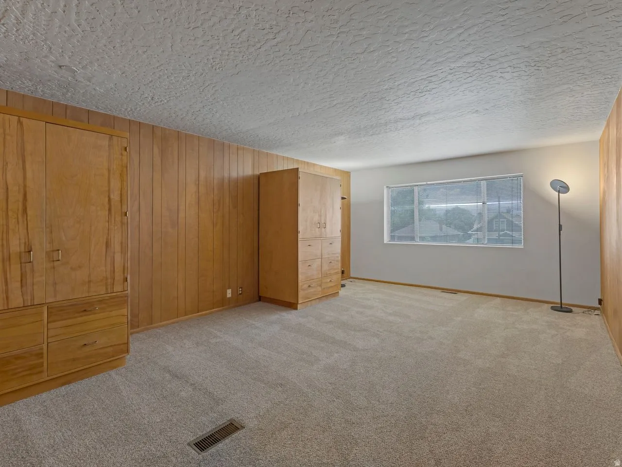 Carpeted room featuring built-in wood cabinetry, wood paneling, and a large window