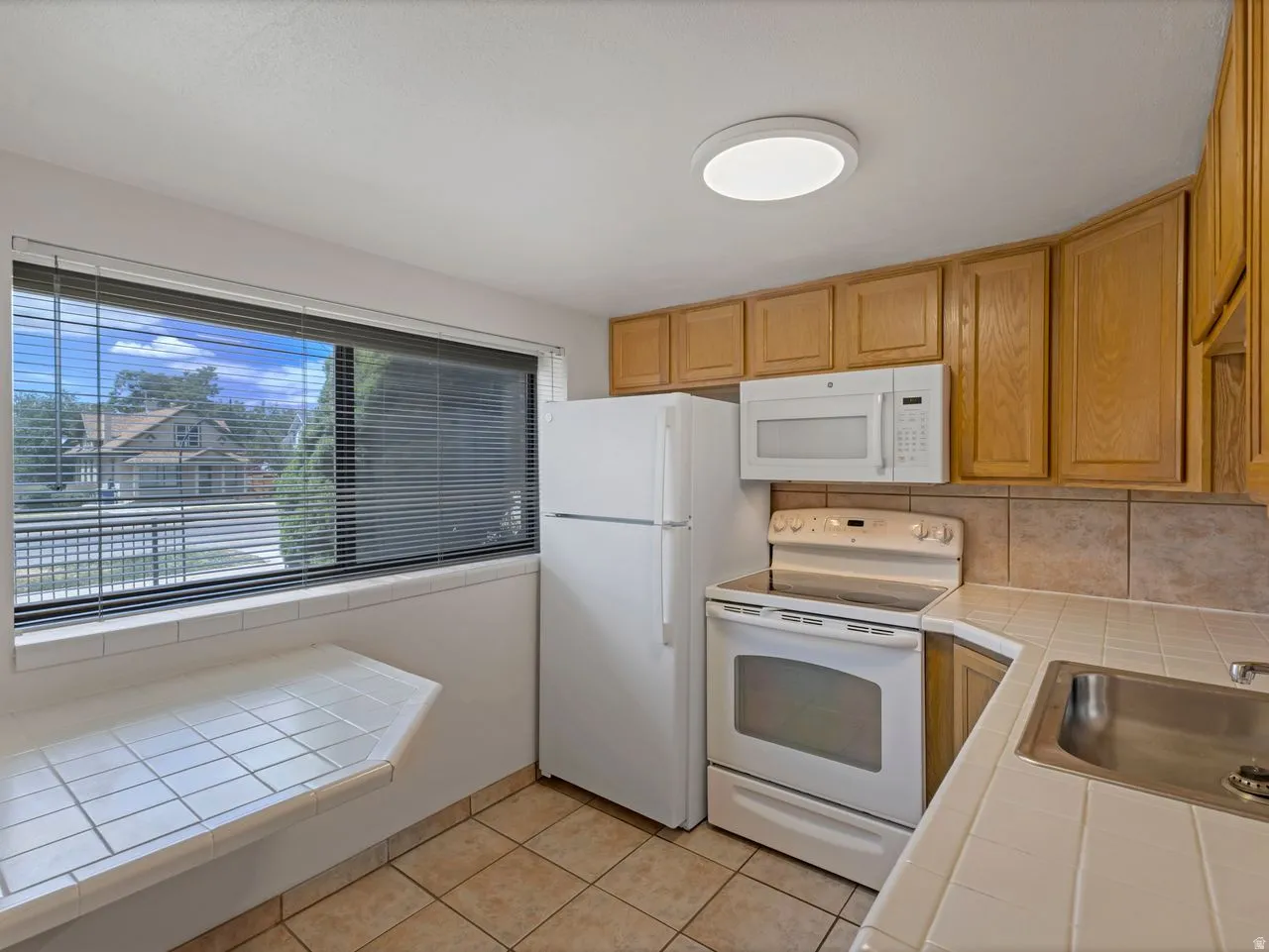 Kitchen featuring wood-finish cabinetry, white appliances, and tiled flooring