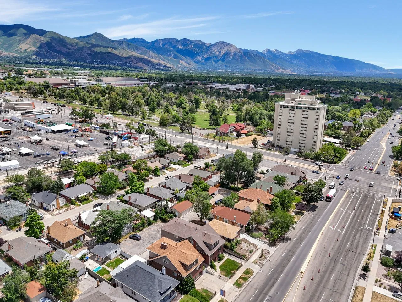 Aerial perspective showcasing a residential area with diverse architectural styles, a multi-lane thoroughfare, and a distant mountain range backdrop