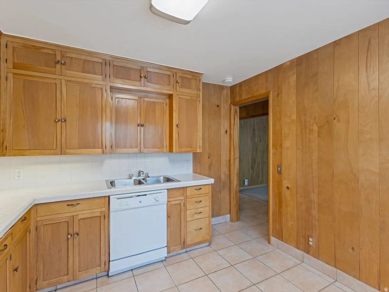 Kitchen featuring wood cabinetry, white countertops, a double basin stainless steel sink, and a white dishwasher