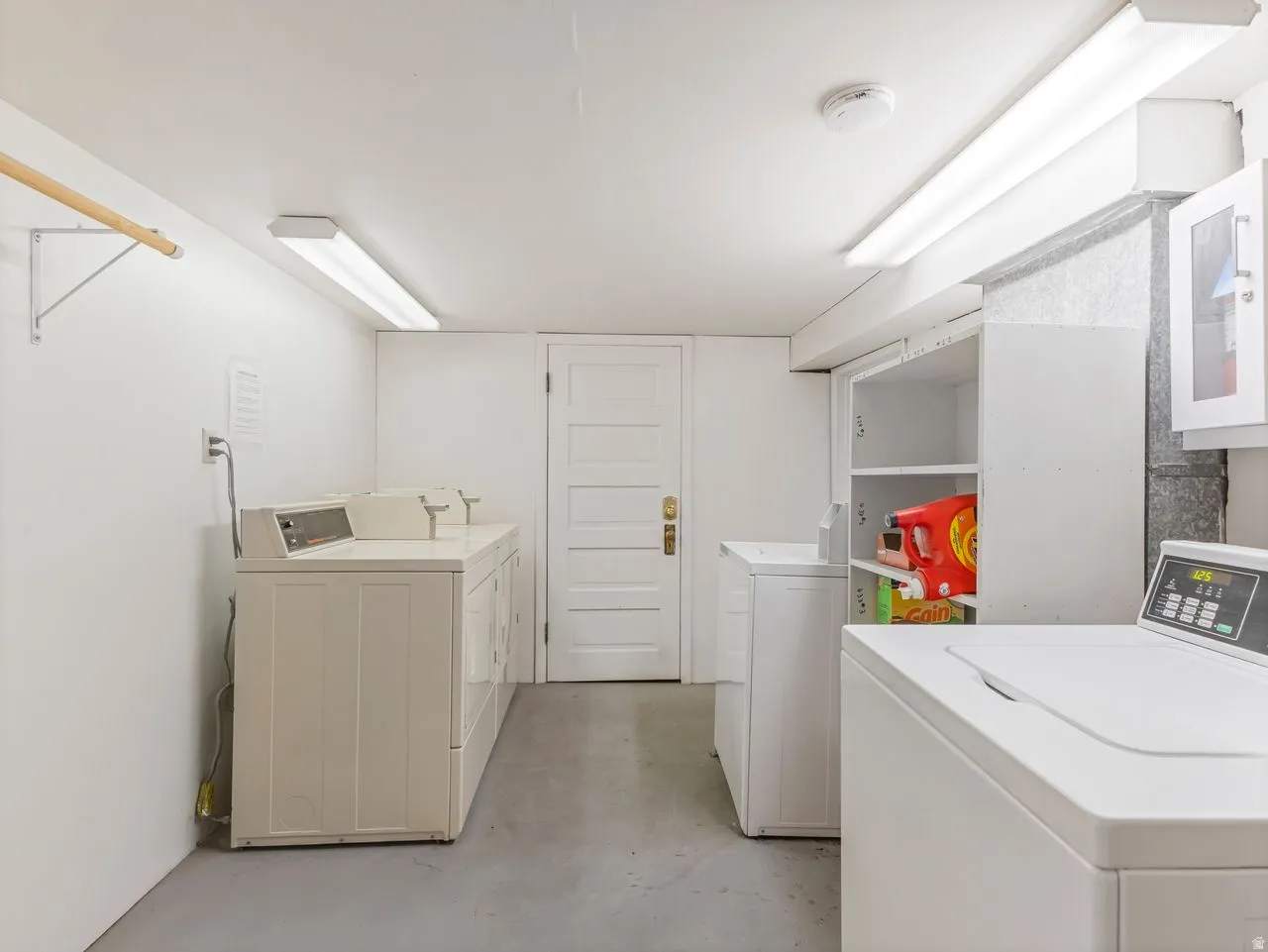 Dedicated laundry room featuring multiple washing machines, built-in shelving, and overhead fluorescent lighting
