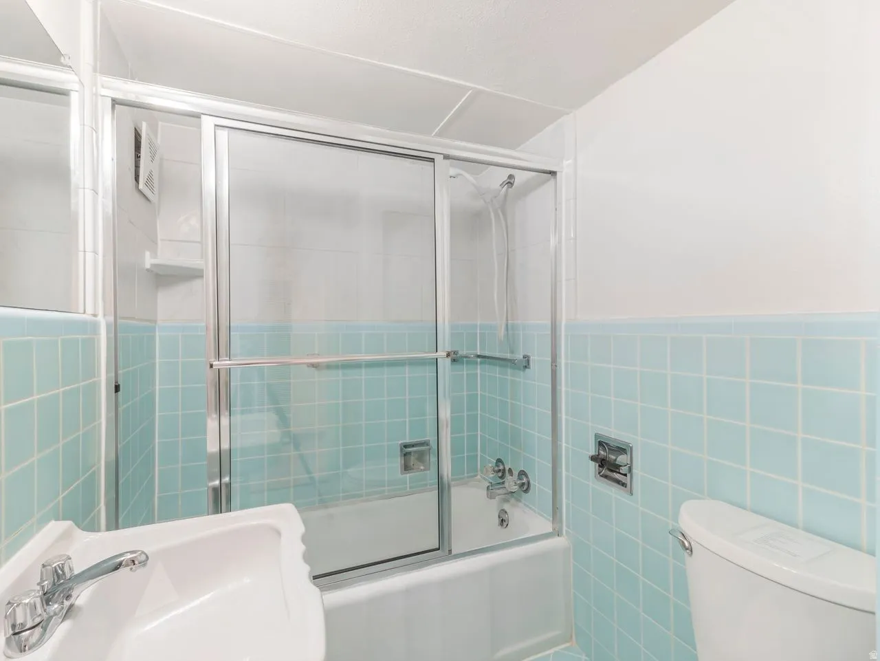 Bathroom featuring a bathtub with a sliding glass enclosure, white porcelain sink with chrome faucet, and a toilet with chrome hardware