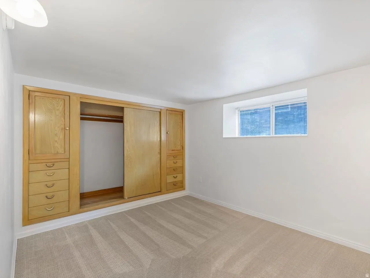 Recessed window with white trim, built-in wooden cabinetry, integrated drawers, sliding closet doors, and plush carpet flooring