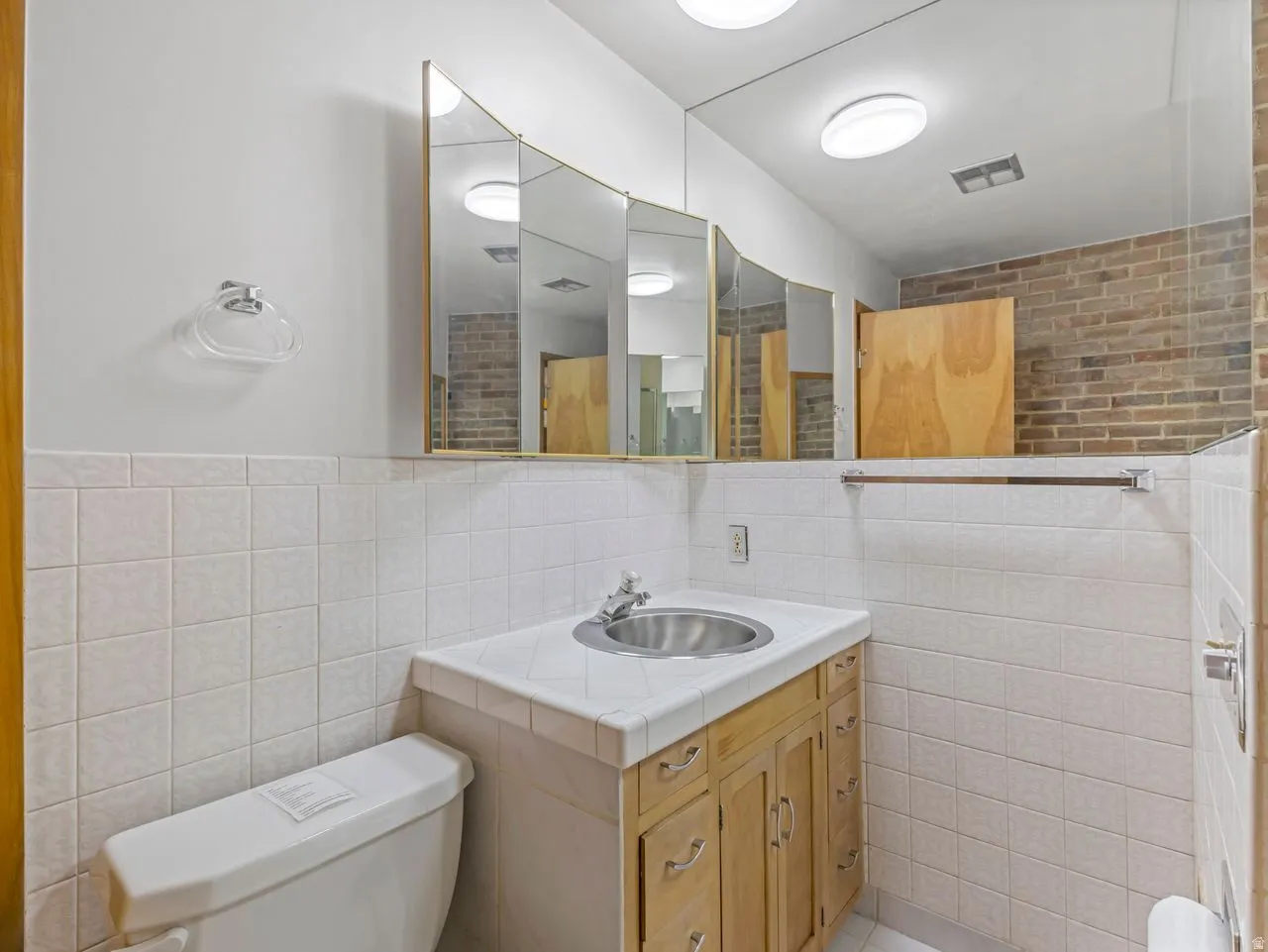 Bathroom vanity featuring a stainless steel sink, wood-finish cabinetry, and a tile countertop