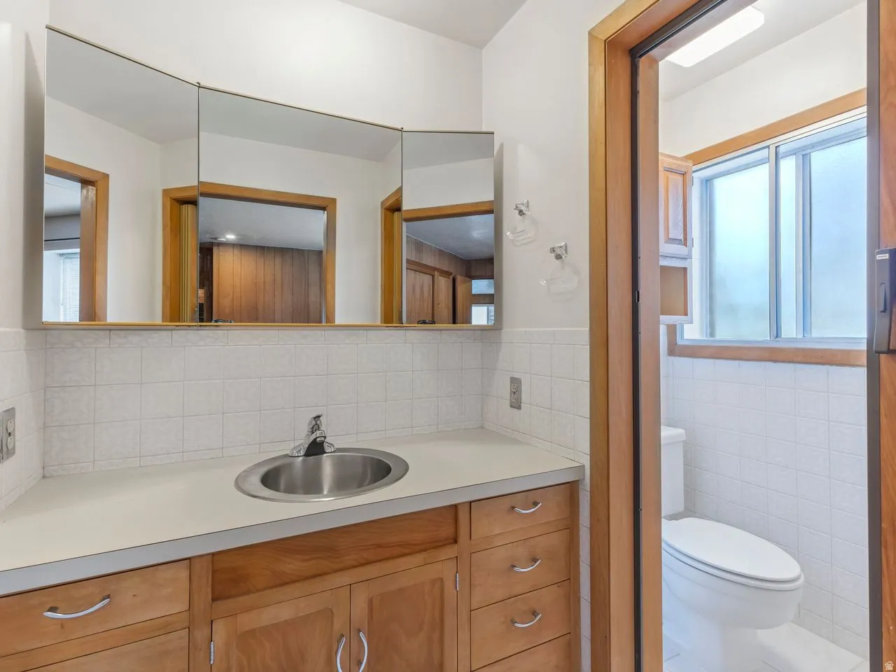 Vanity with wood cabinetry, an integrated stainless steel sink, and a light-toned countertop