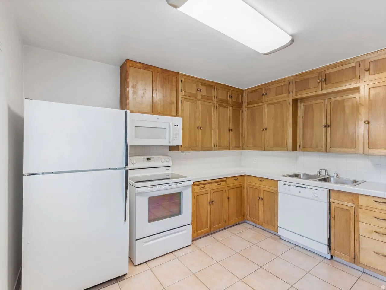 Kitchen featuring wood-finish cabinetry, white appliances, dual basin sink, white countertops, and tiled flooring