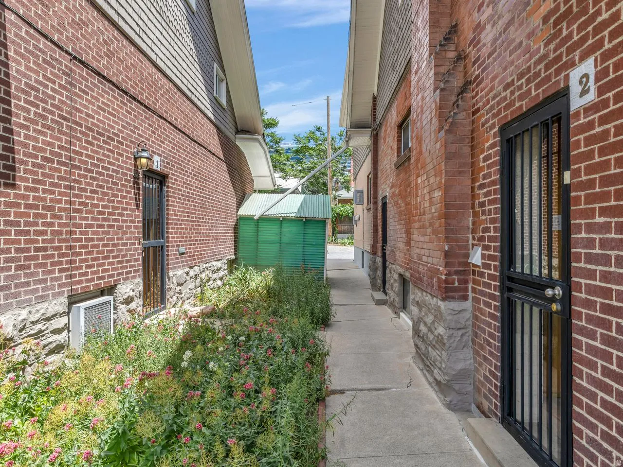 Brick exterior with stone foundation, featuring a concrete walkway and wrought iron security doors
