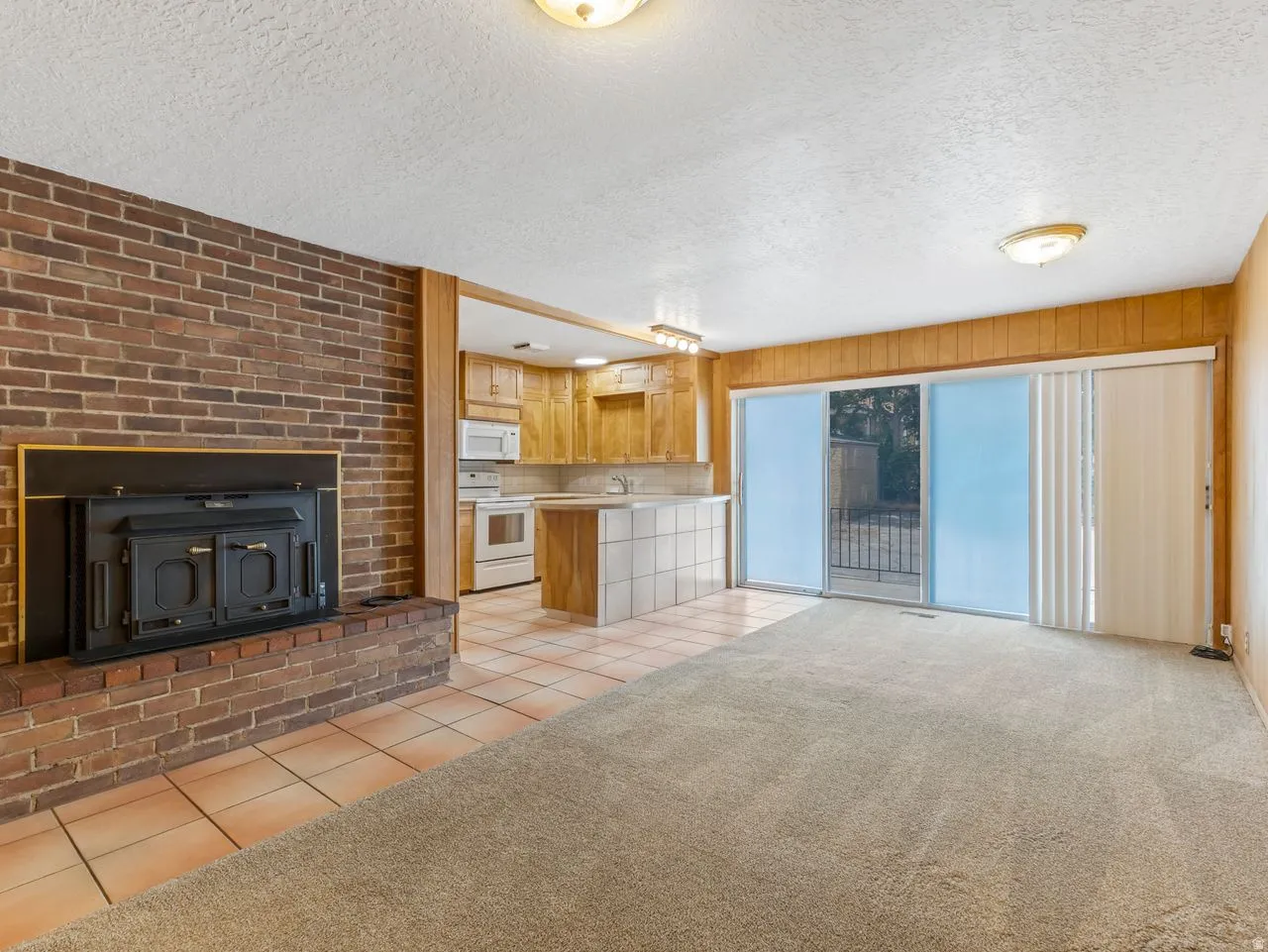 Living area featuring a brick fireplace with a black insert, light-toned carpeting, and a sliding glass door