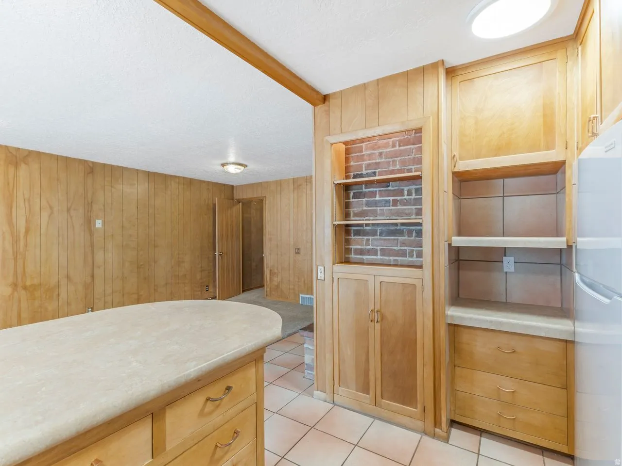 Kitchen area featuring wood-finish cabinetry, a built-in brick-backed shelving unit, and a tile floor