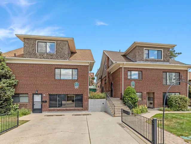 Brick facade exterior featuring dormer windows with shingle siding, a paved driveway, and mature landscaping