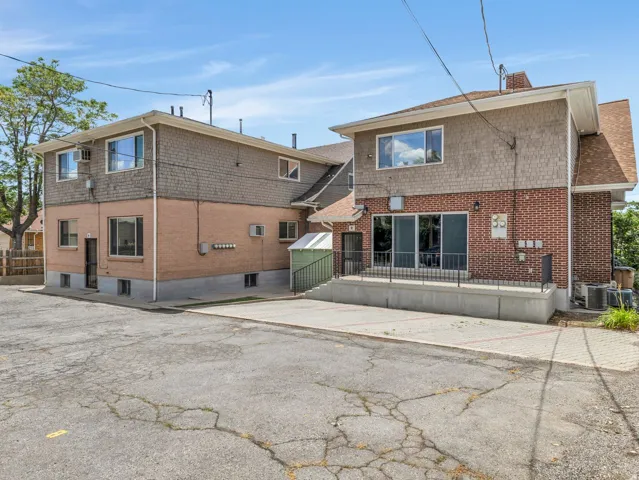 Two-story structure featuring brick and shake siding, multiple windows, a ground-level patio with black railings, and a lower-level entrance with a screened door