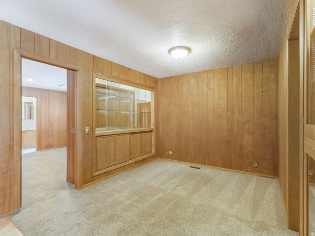Interior room featuring wood paneling throughout, a built-in display cabinet with glass shelving and lower cabinetry, and textured ceiling