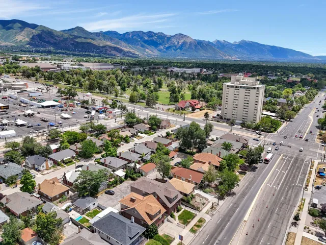 Aerial perspective showcasing a residential area with diverse architectural styles, a multi-lane thoroughfare, and a distant mountain range backdrop
