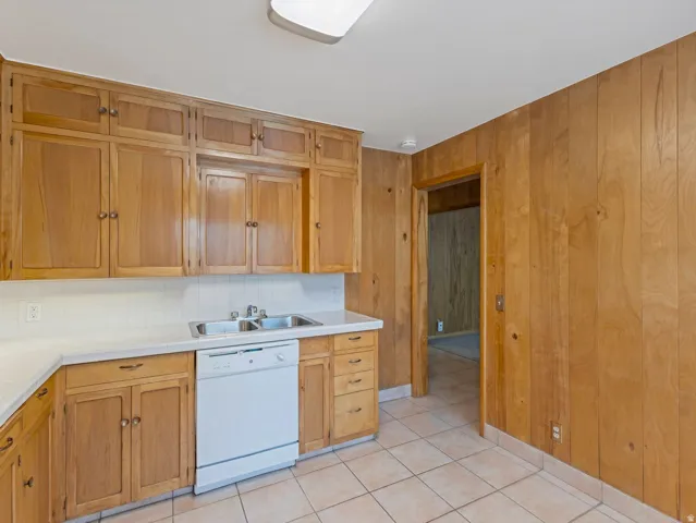 Kitchen featuring wood cabinetry, white countertops, a double basin stainless steel sink, and a white dishwasher