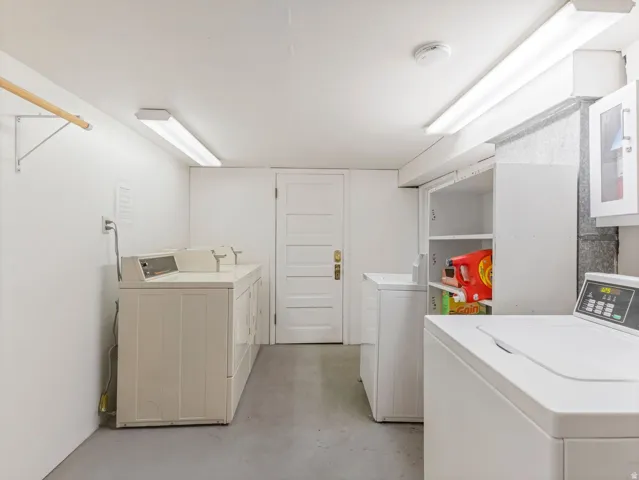 Dedicated laundry room featuring multiple washing machines, built-in shelving, and overhead fluorescent lighting
