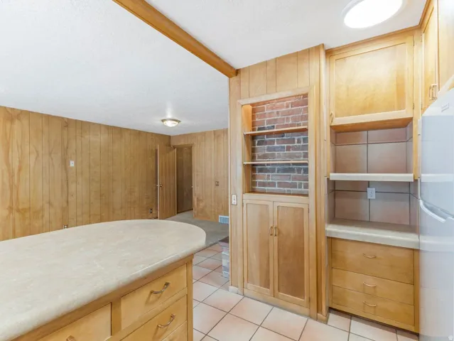 Kitchen area featuring wood-finish cabinetry, a built-in brick-backed shelving unit, and a tile floor