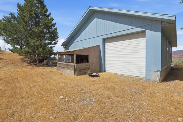 Detached structure featuring blue siding, a white roll-up garage door, and an attached wooden enclosure