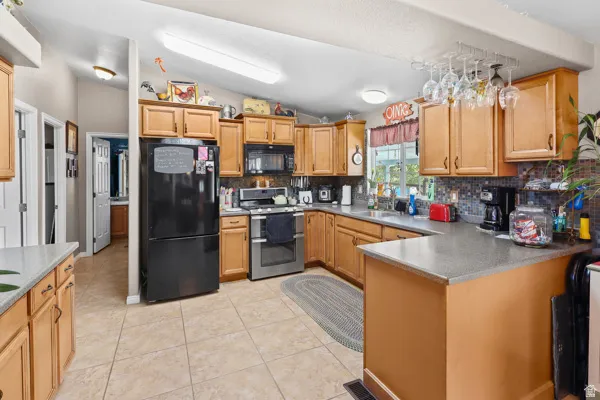 Kitchen featuring light wood cabinetry, a mosaic tile backsplash, black and stainless steel appliances, a breakfast bar, and tile flooring