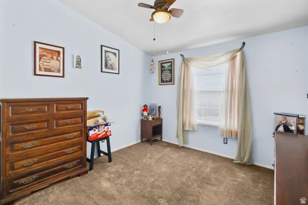 Spacious room featuring light blue walls, brown carpet flooring, a ceiling fan with integrated lighting, and a window with blinds