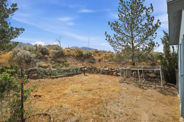 Expansive outdoor space featuring a stone retaining wall, mature trees, and a mountain backdrop