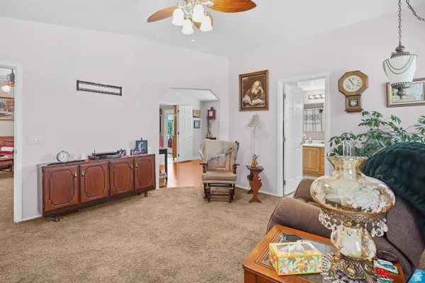 Expansive carpeted living space featuring a ceiling fan with integrated lighting, arched doorways, and a wood-finish console cabinet
