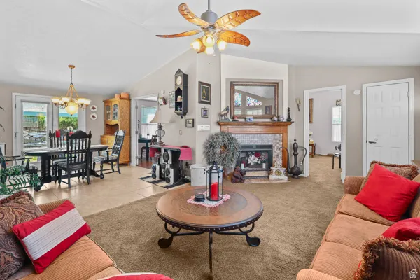 Vaulted ceiling with a ceiling fan light fixture, tiled fireplace surround with a wood mantel, and a dining area with a chandelier