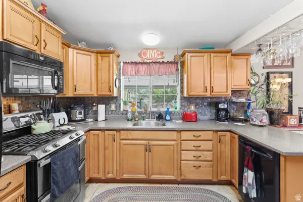 Kitchen featuring light wood cabinetry, dark countertops, built-in black microwave, stainless steel gas range, and a mosaic tile backsplash