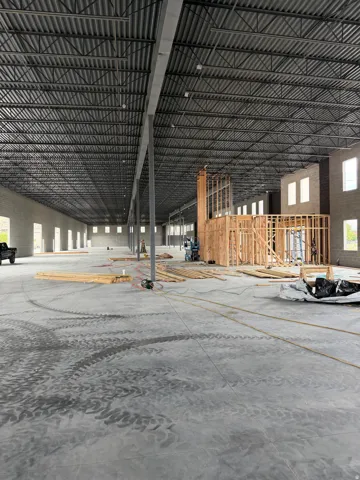 Expansive industrial space featuring a high truss ceiling system, concrete flooring, and multiple window openings for natural light