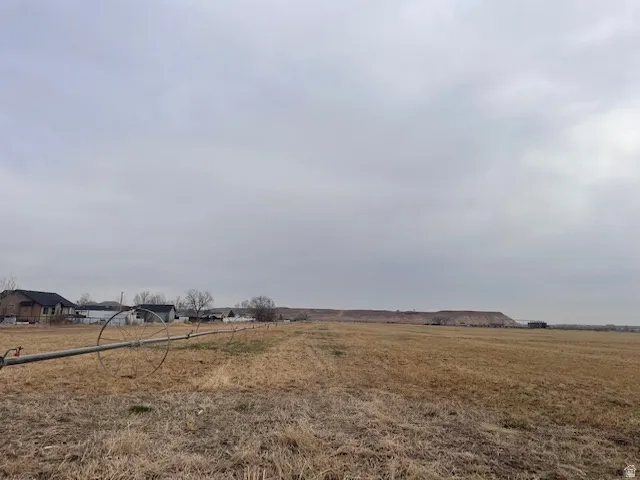Expansive agricultural land featuring a visible irrigation system and distant structures, framed by a prominent hillside