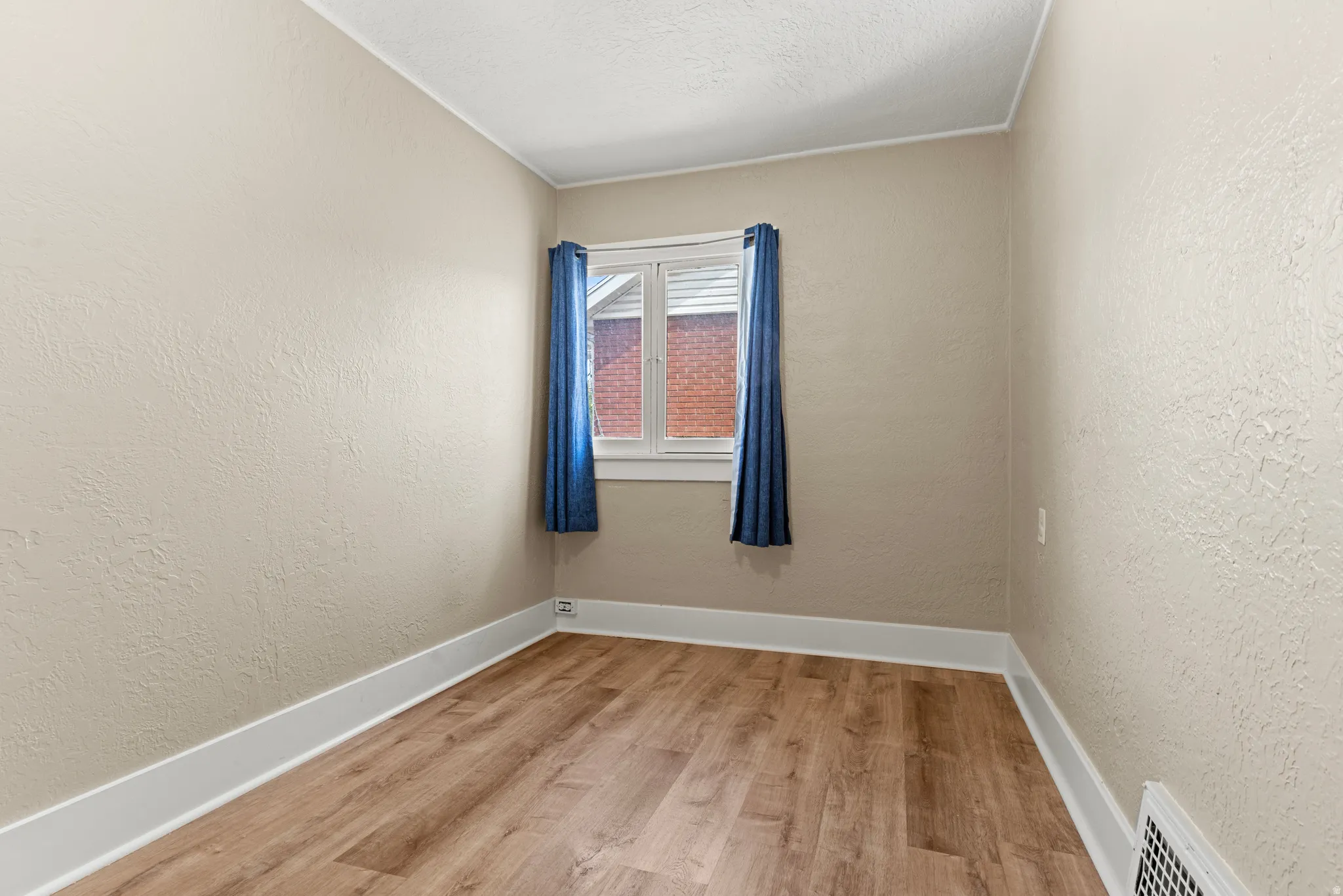 Neutral-toned room with wood-finish flooring, white baseboards, and textured walls