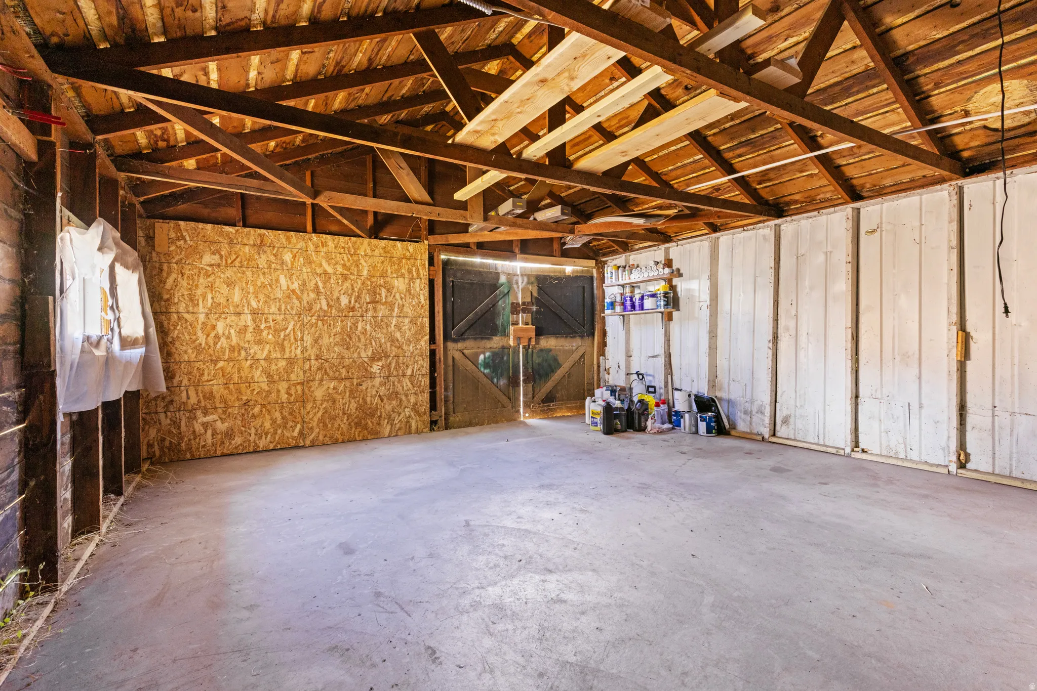 Spacious garage interior featuring exposed wood beam ceiling, concrete flooring, and double-door entry