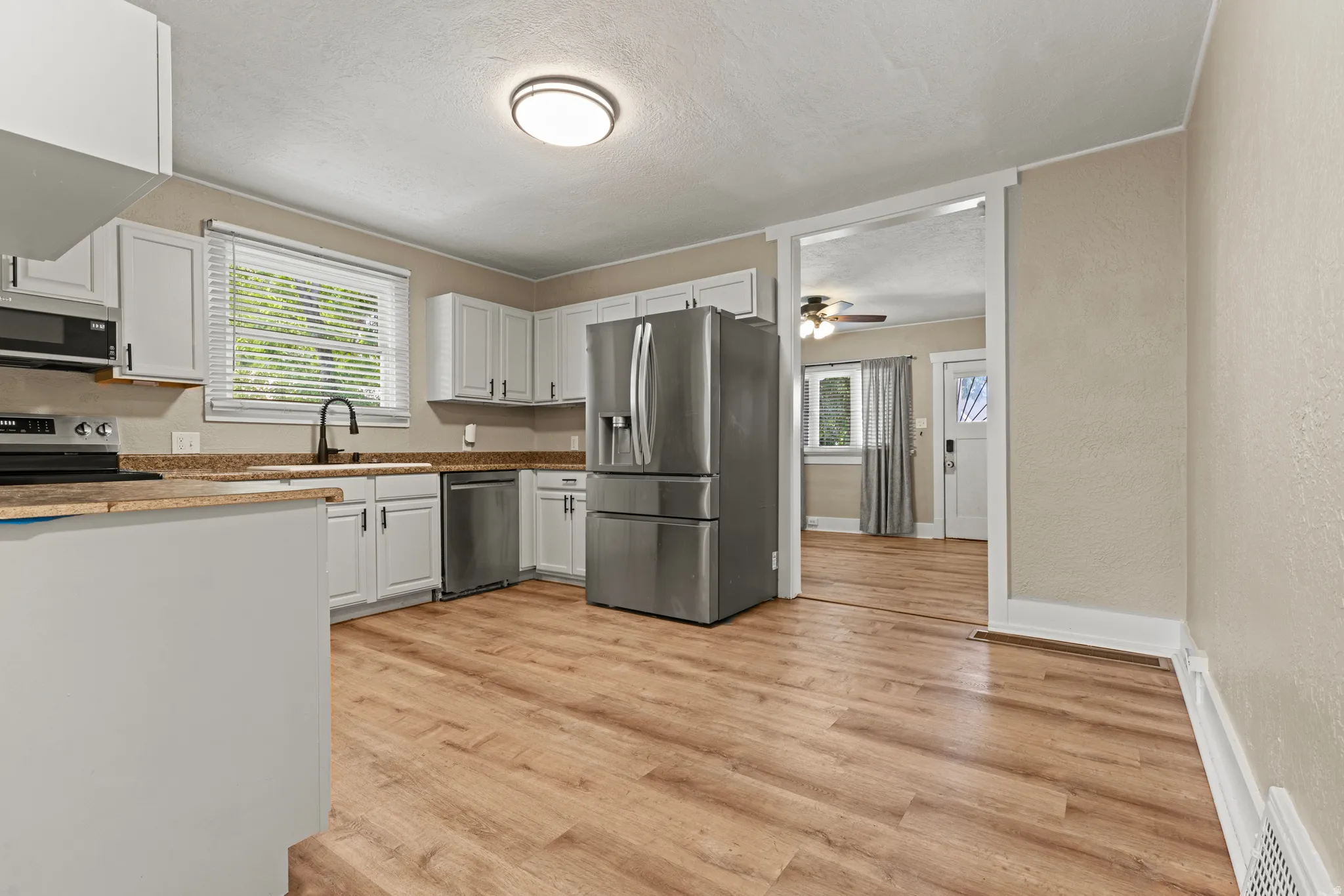 Contemporary kitchen featuring wood-finish flooring, white cabinetry with black hardware, a stainless steel refrigerator, and a granite-style countertop