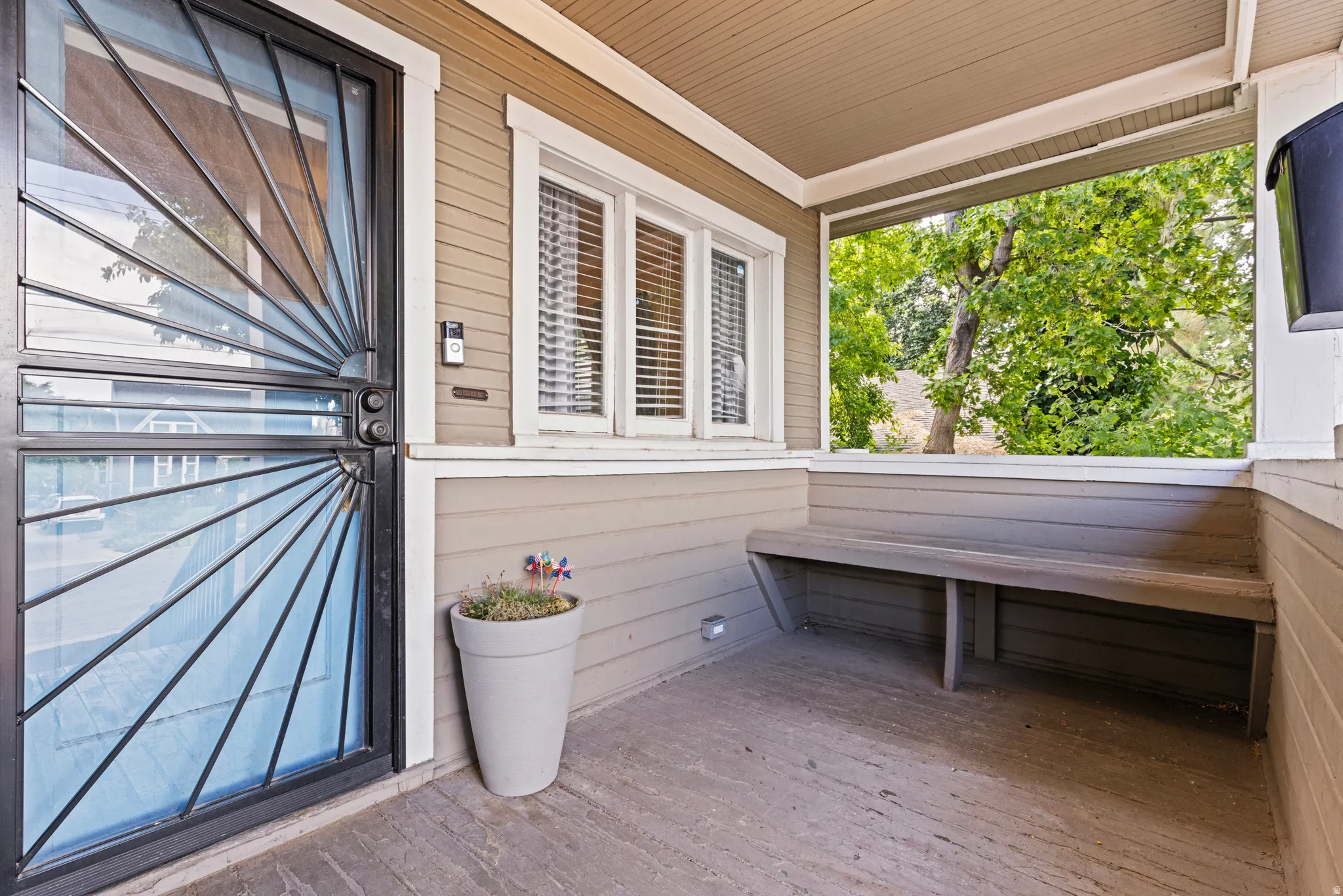 Covered front porch featuring a decorative security door, built-in wooden bench, and exterior wall siding