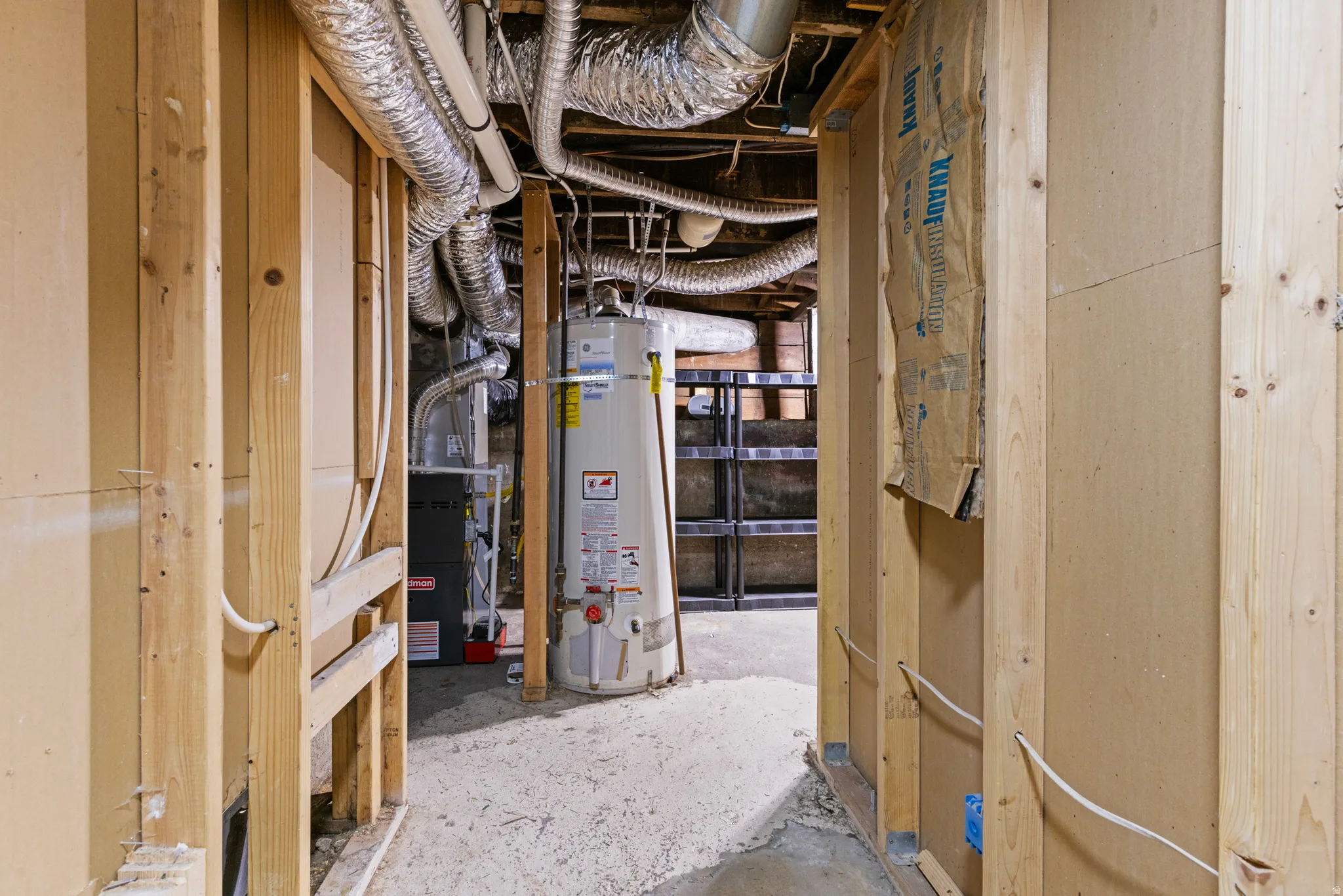 Unfinished basement area featuring exposed wood framing, ductwork, and utility systems including a water heater and furnace