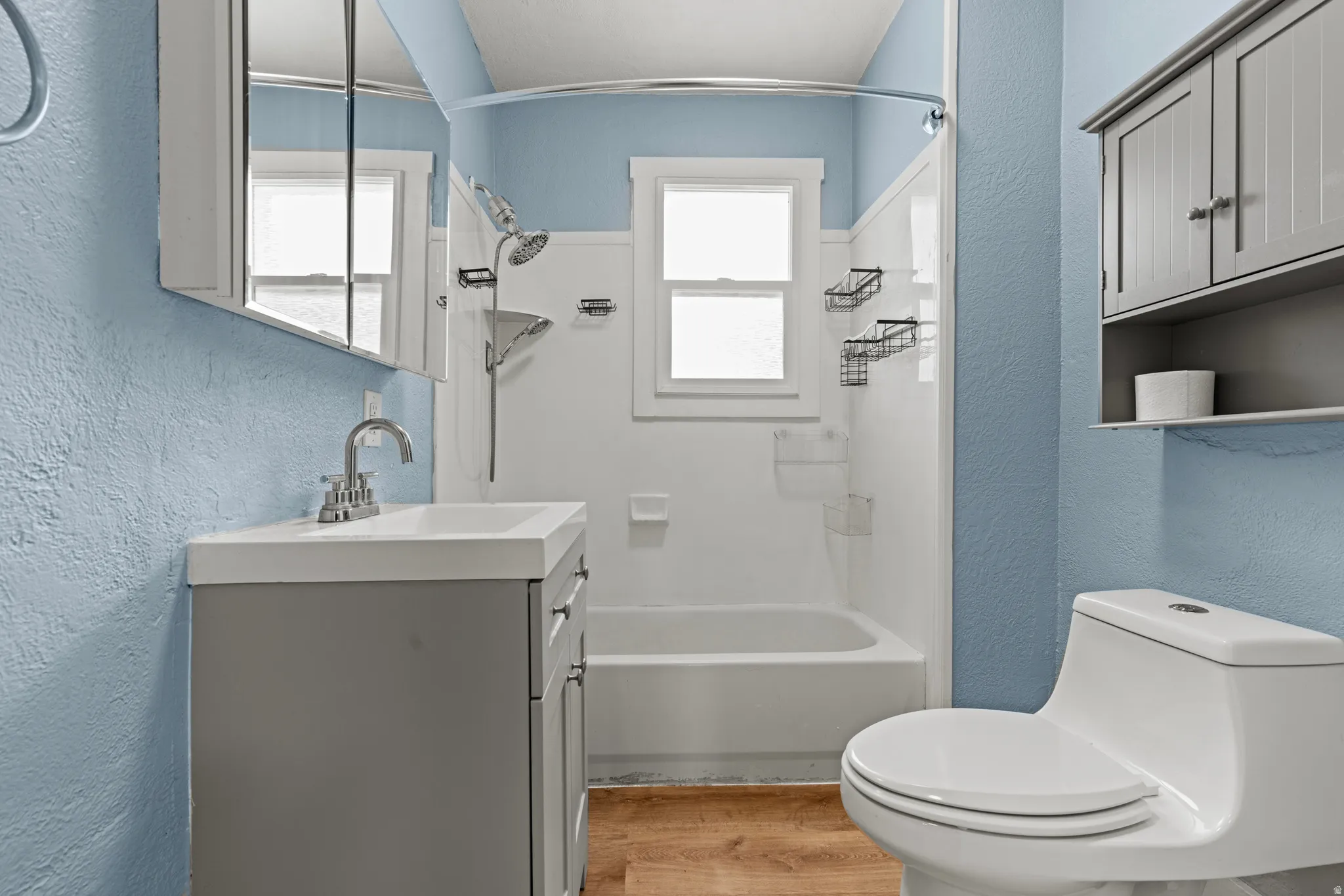 Bathroom featuring a vanity with integrated sink, chrome faucet, medicine cabinet, and wood-finish flooring