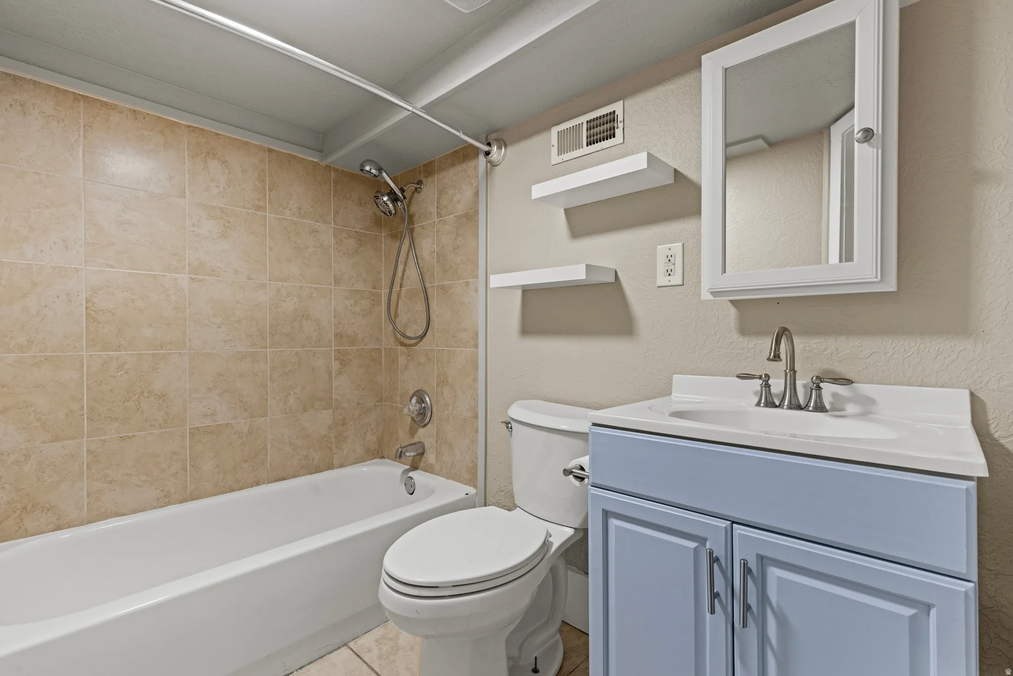 Bathroom featuring a white bathtub, beige tiled shower surround, toilet, light blue vanity with a white countertop and basin sink, and a mirrored medicine cabinet