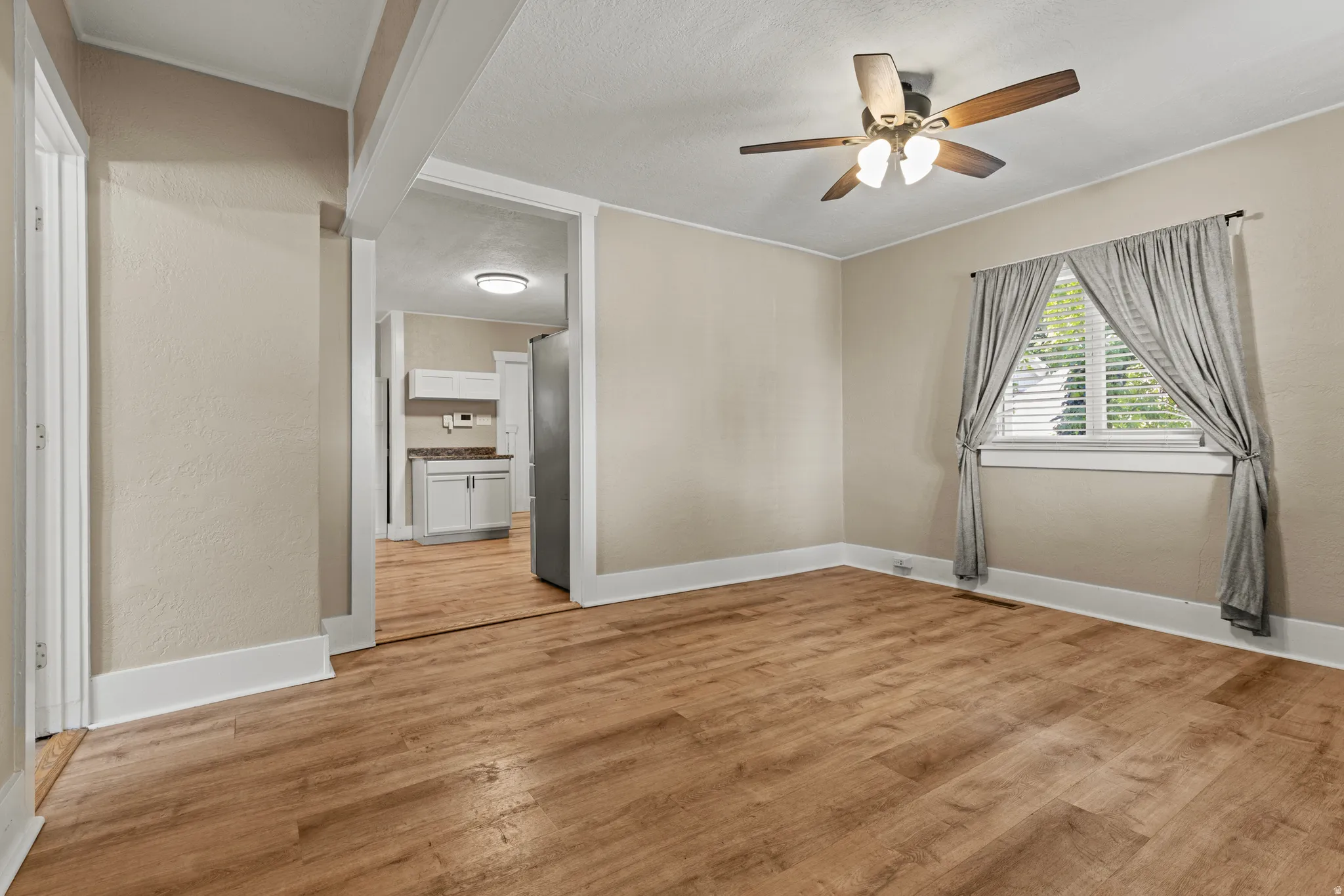 Open living area featuring wood-finish flooring, neutral paint, a ceiling fan, and a window with blinds