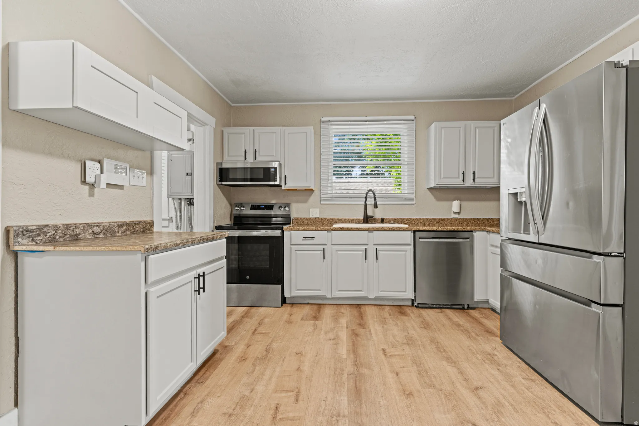 Kitchen featuring white shaker-style cabinetry, wood-finish flooring, stainless steel appliances, and a window with blinds