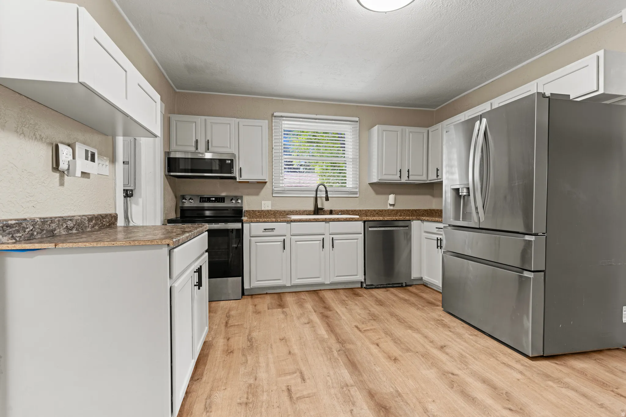 Kitchen featuring light wood-finish flooring, white cabinetry with black hardware, stainless steel appliances, and a window with blinds