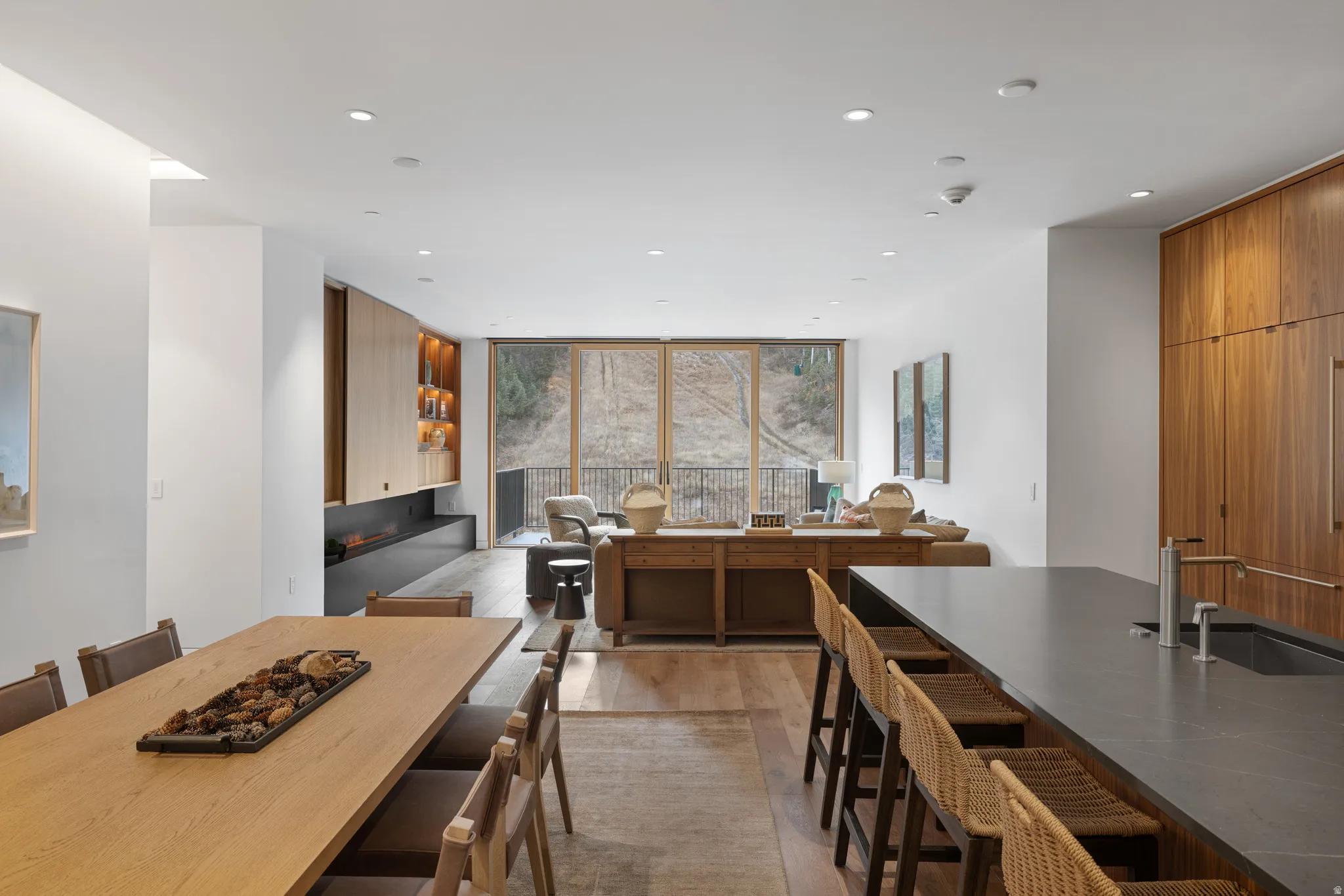 Open-concept interior featuring light wood-finish flooring, a linear fireplace with a dark finish, and full-height windows