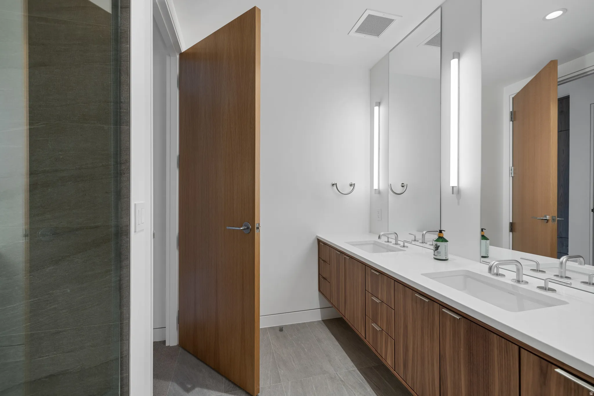 Modern bathroom featuring a dual vanity with white countertops, integrated sinks, and wood-finish cabinetry