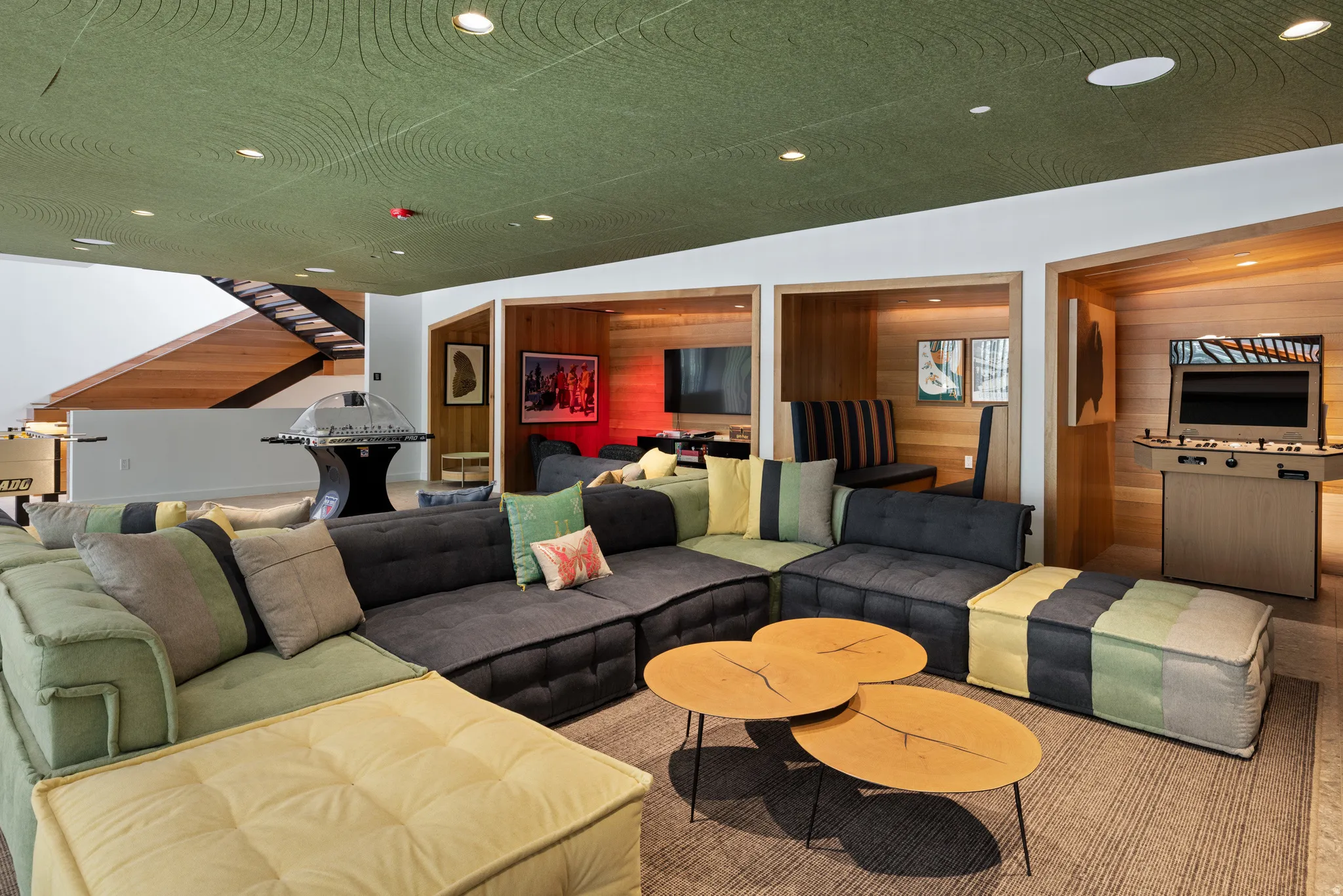 Entertainment space featuring a green textured ceiling with recessed lighting, built-in wood-paneled nooks, and a contemporary wood staircase with black metal railing