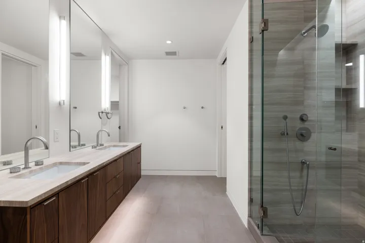 Modern bathroom featuring a dual vanity with a light-toned countertop, under-cabinet lighting, and a full-length mirror