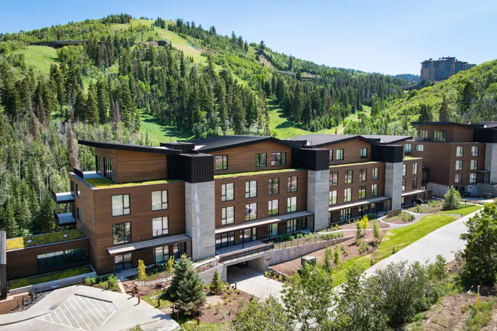 Modern multi-story building featuring wood-finish siding, concrete structural elements, and a green roof system
