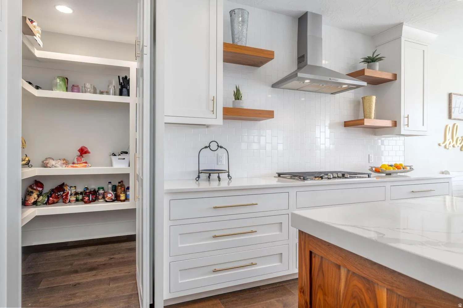 Modern kitchen featuring white shaker cabinetry with gold-tone hardware, white subway tile backsplash, and a stainless steel range hood