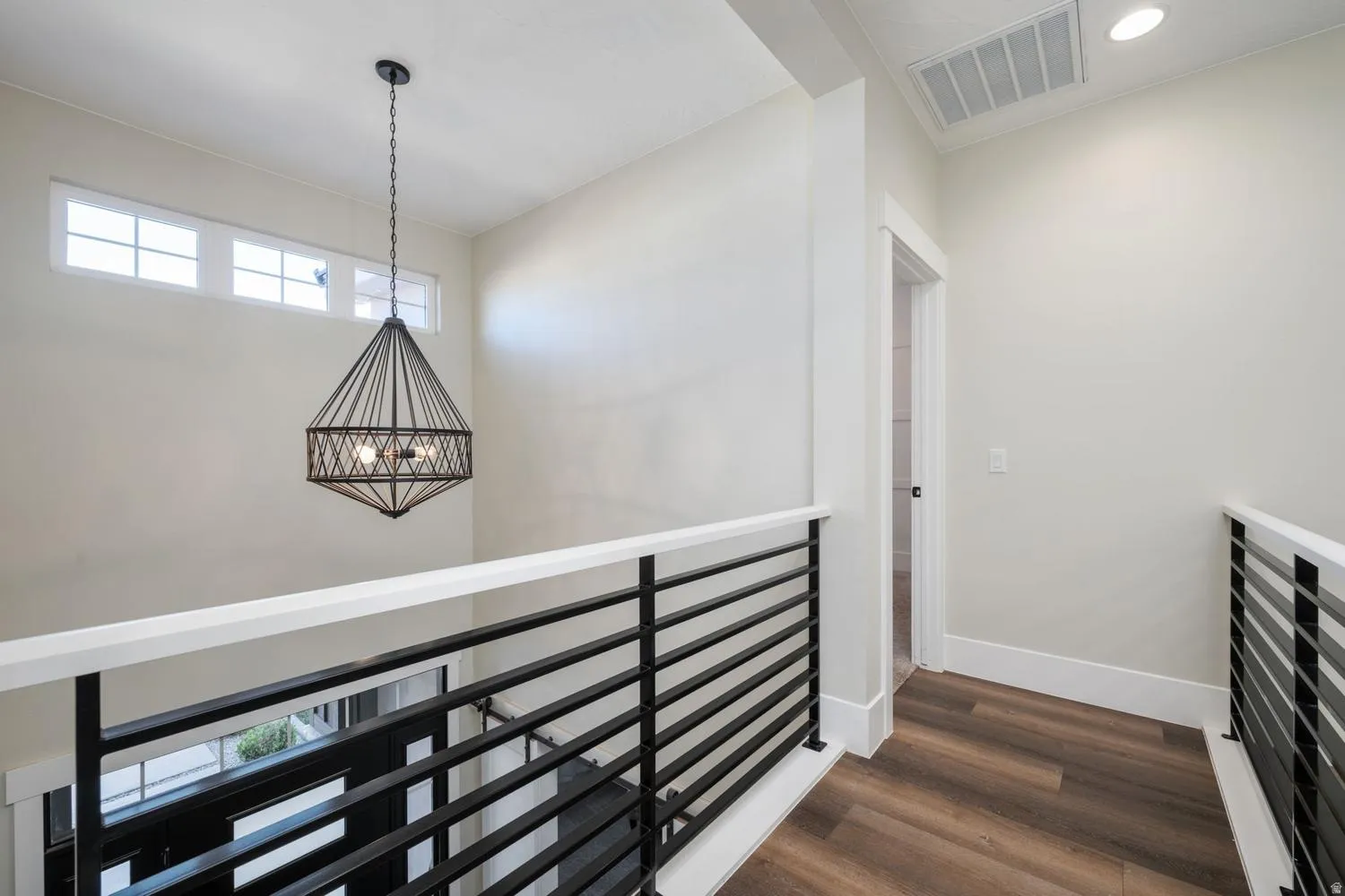 Upper-level hallway featuring wood-finish flooring, a contemporary black metal chandelier, and white walls with transom windows