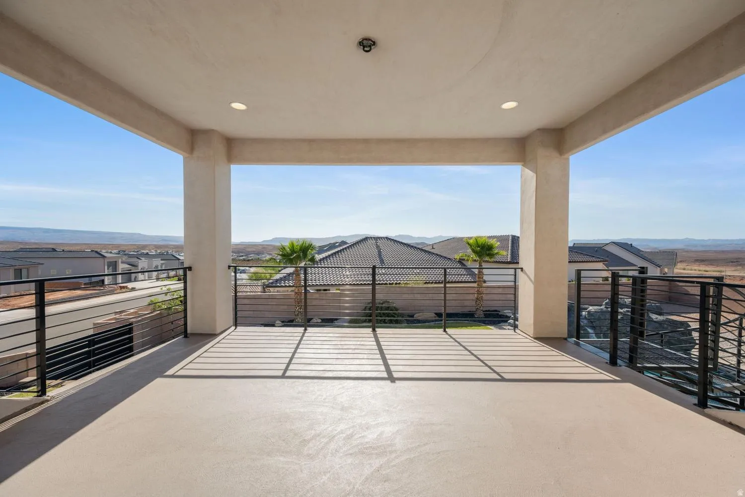 Spacious covered patio featuring a concrete floor, recessed lighting, and black metal railings
