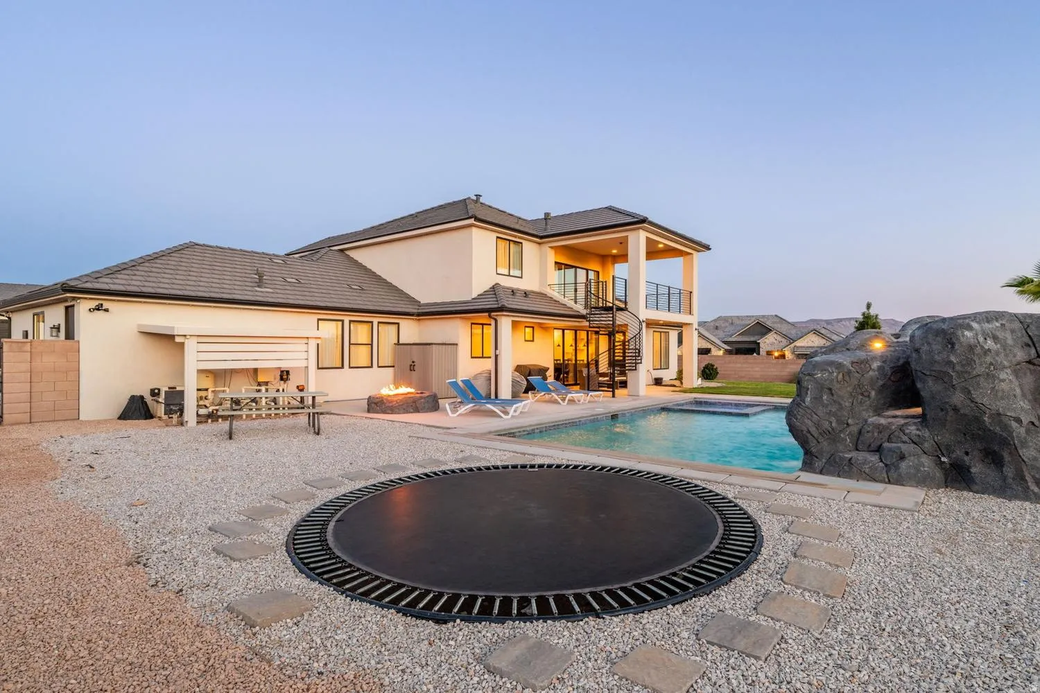 Spacious backyard featuring a rectangular swimming pool with integrated spa, a fire pit area, and a spiral staircase leading to a second-story balcony