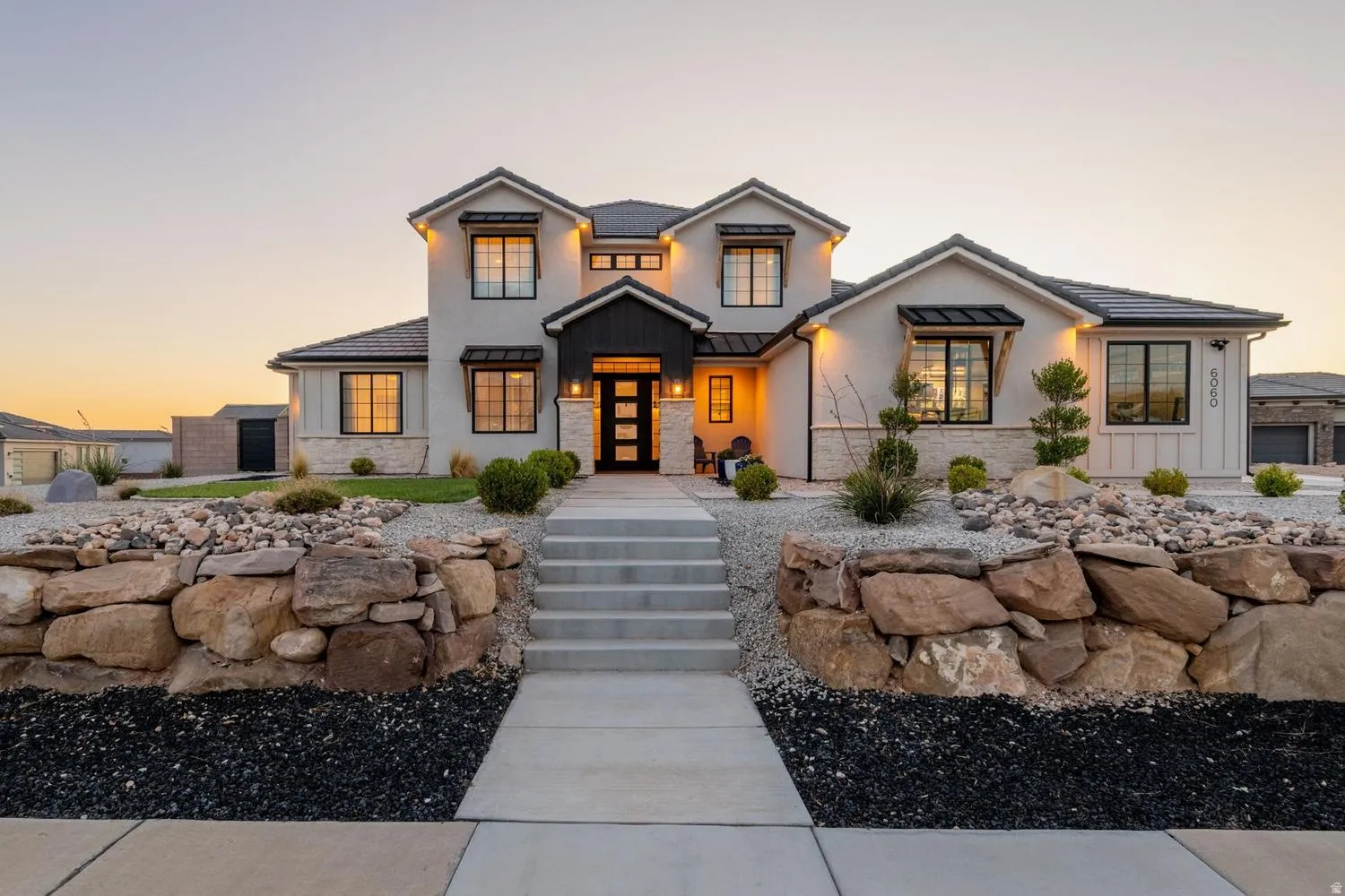 Contemporary two-story residence featuring a stucco and stone exterior, a dark tile roof, and prominent dormer windows